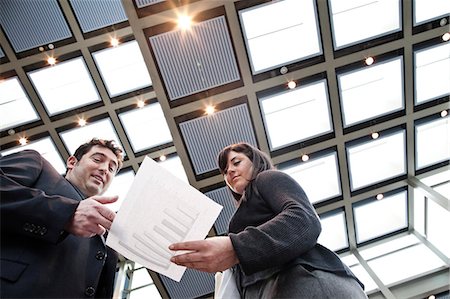 simsearch:6118-09173926,k - Two business people going over paperwork in a large convention centre lobby. Stock Photo - Premium Royalty-Free, Code: 6118-09173931