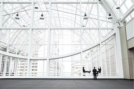 simsearch:6118-09173926,k - Three businesspeople meeting in front of a window in a large convention centre loggy. Stock Photo - Premium Royalty-Free, Code: 6118-09173932