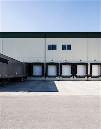 Exterior view of a warehouse loading dock with a truck trailer pulled up to one of the doors. Stock Photo - Premium Royalty-Free, Code: 6118-09174171