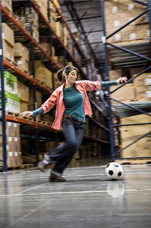 simsearch:6118-09174228,k - A Caucasian female about to kick a soccer ball during a work break in a distribution warehouse. Fotografie stock - Premium Royalty-Free, Codice: 6118-09174190