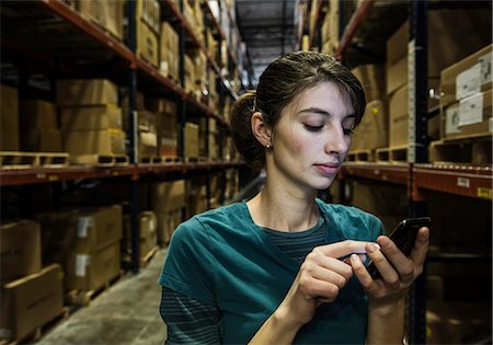 simsearch:6118-09174228,k - A Caucasian female warehouse worker checking her phone for texts while standing in a distribution warehouse. Fotografie stock - Premium Royalty-Free, Codice: 6118-09174192