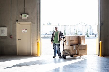 simsearch:6118-09174220,k - Male warehouse worker standing next to a manual pallet jack and cardboard boxes in a distribution warehouse. Fotografie stock - Premium Royalty-Free, Codice: 6118-09174199