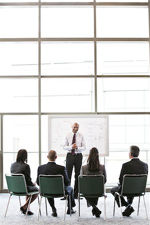 simsearch:6118-09173926,k - A small group of business people sitting and watching a presentation around a white board in front of a large office window. Stock Photo - Premium Royalty-Free, Code: 6118-09174111