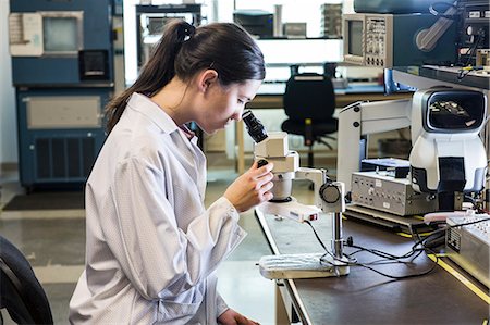 simsearch:6118-09174461,k - A Caucasian female technician using a microscope to examine a part in a technical research and development site. Stockbilder - Premium RF Lizenzfrei, Bildnummer: 6118-09174134