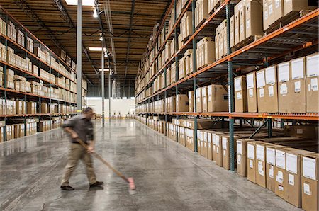 simsearch:6118-09174228,k - An employee sweeping the floor of an aisle between large racks of storage boxes in a distribution warehouse. Fotografie stock - Premium Royalty-Free, Codice: 6118-09174241