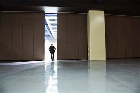 simsearch:6118-09174347,k - Businessman standing in a doorway between rooms in a convention centre arena. Fotografie stock - Premium Royalty-Free, Codice: 6118-09174262