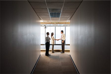 simsearch:6118-09173536,k - A mixed race group of business people talking and shaking hands in front of a window at the end of a long hallway. Stockbilder - Premium RF Lizenzfrei, Bildnummer: 6118-09174289