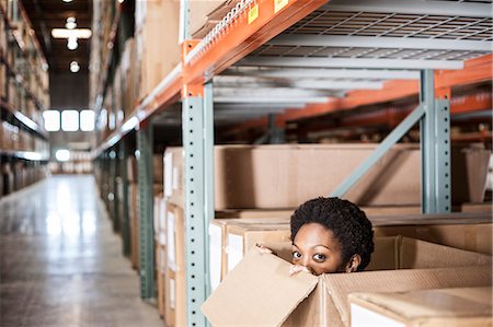 simsearch:6118-09174220,k - A black female worker hiding inside a cardboard box in a distribution warehouse. Fotografie stock - Premium Royalty-Free, Codice: 6118-09174202