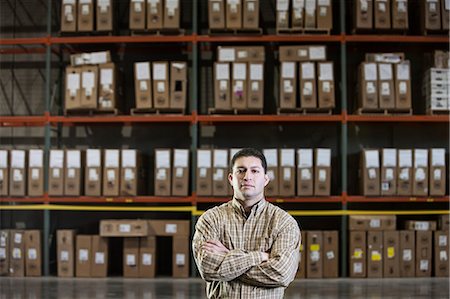simsearch:6118-09174347,k - A Hispanic male warehouse worker standing next to racks of boxed products in a distribution warehouse. Fotografie stock - Premium Royalty-Free, Codice: 6118-09174206