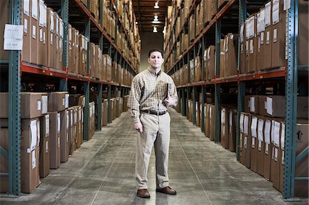 simsearch:6118-09174347,k - A Hispanic male warehouse worker standing next to racks of boxed products in a distribution warehouse. Fotografie stock - Premium Royalty-Free, Codice: 6118-09174209