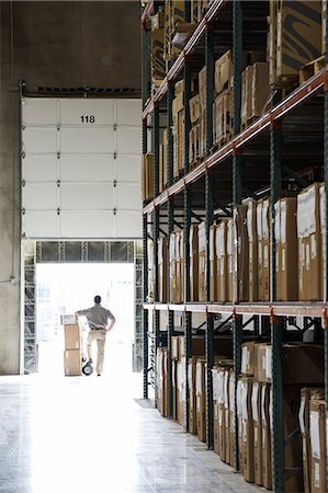 simsearch:700-05389538,k - An employee with a hand truck full of boxes standing in a loading dock door in a large distribution warehouse. Photographie de stock - Premium Libres de Droits, Code: 6118-09174226