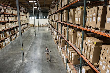simsearch:6118-09174220,k - A view from above looking down on a warehouse worker checking inventory of boxes on racks in a distribution warehouse. Fotografie stock - Premium Royalty-Free, Codice: 6118-09174238