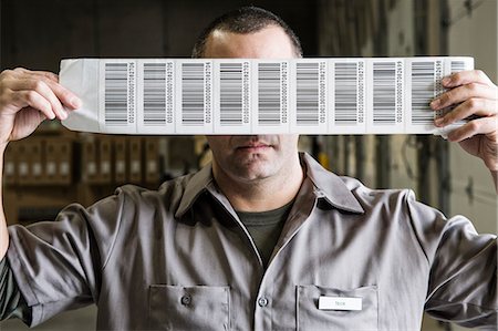 simsearch:6118-09174220,k - A warehouse worker holding up a sheet of bar code shipping labels in a distribution warehouse. Fotografie stock - Premium Royalty-Free, Codice: 6118-09174239