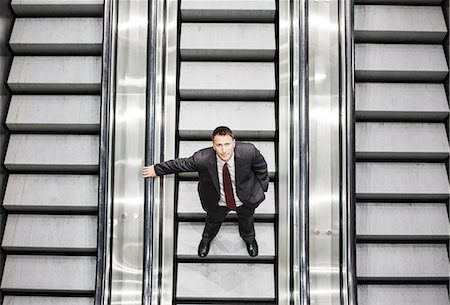 simsearch:6118-09174347,k - Looking down on a Caucasian businessman looking up while riding an escalator in a convention centre. Fotografie stock - Premium Royalty-Free, Codice: 6118-09174351