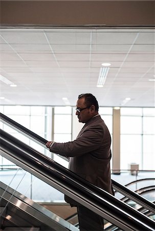 simsearch:6118-09174347,k - A Hispanic businessman checking his notebook computer while going up an escalator in a convention centre space. Fotografie stock - Premium Royalty-Free, Codice: 6118-09174357