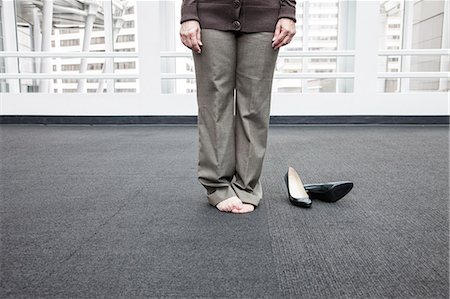 Low closeup view of a businesswoman standing on a carpet in bare feet. Stock Photo - Premium Royalty-Free, Code: 6118-09174355