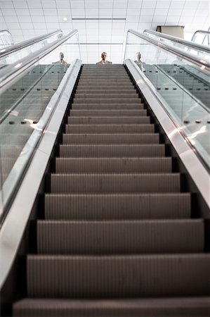 simsearch:6118-09174347,k - Looking up an escalator with a person about to get on the escalator in a convention centre space. Fotografie stock - Premium Royalty-Free, Codice: 6118-09174356