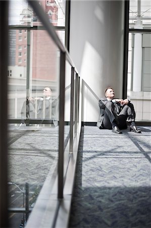 simsearch:6118-09174347,k - Low view looking at a Caucasian businessman taking a break sitting at the base of a column in a convention centre space. Fotografie stock - Premium Royalty-Free, Codice: 6118-09174360