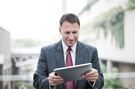 simsearch:6118-09174347,k - A Caucasian businessman checking his notebook computer while standing in a convention cener lobby. Fotografie stock - Premium Royalty-Free, Codice: 6118-09174372