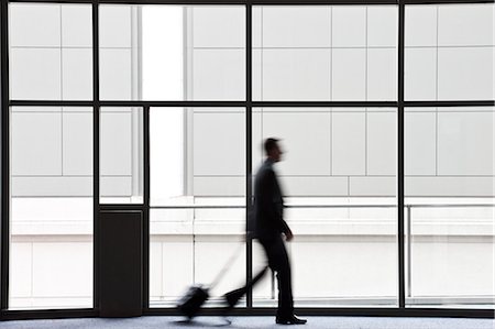 simsearch:6118-09174347,k - A businessman blurred in silhouette while walking past a large window in a convention centre lobby. Fotografie stock - Premium Royalty-Free, Codice: 6118-09174380