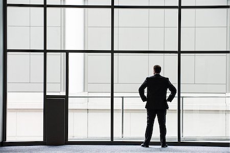 simsearch:6118-09174347,k - A businessman in silhouette standing at a large window in a convention centre lobby. Fotografie stock - Premium Royalty-Free, Codice: 6118-09174381