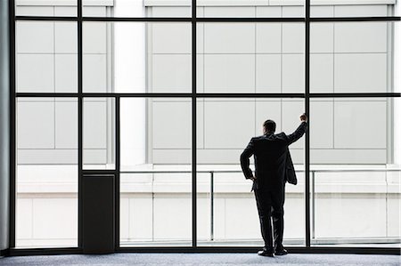 simsearch:6118-09174347,k - A businessman in silhouette standing at a large window in a convention centre lobby. Fotografie stock - Premium Royalty-Free, Codice: 6118-09174382