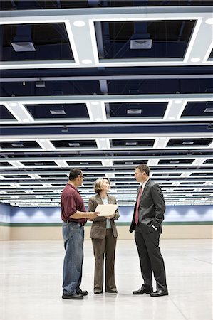 simsearch:6118-09129521,k - Three business meeting planners talking on the floor of a convention centre space. Stock Photo - Premium Royalty-Free, Code: 6118-09174387