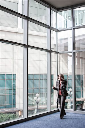simsearch:6118-09174347,k - A Caucasian businesswoman talking on a cell phone while standing next to a large window in a convention centre lobby. Fotografie stock - Premium Royalty-Free, Codice: 6118-09174393