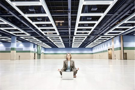 simsearch:6118-09174347,k - A businesswoman in a yoga pose with a laptop computer in the middle of a convention centre arena. Fotografie stock - Premium Royalty-Free, Codice: 6118-09174391