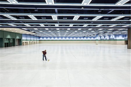 simsearch:6118-09174347,k - A lone man sweeping the floor of a convention centre arena area. Fotografie stock - Premium Royalty-Free, Codice: 6118-09174398
