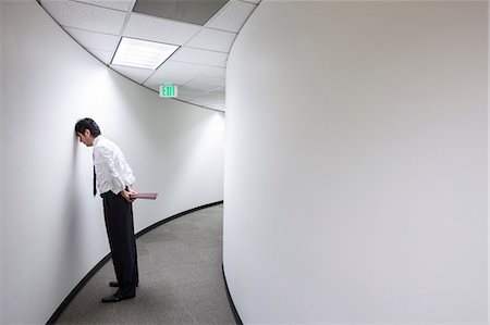 frustrated person at workplace - An Asian businessman frustrated and standing with his head against a wall in a hallway. Stock Photo - Premium Royalty-Free, Code: 6118-09174306