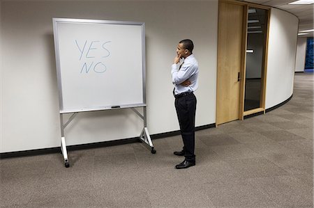 simsearch:649-08084769,k - A black businessman thinking and standing in front of an office white board with the words Yes and No written on it. Foto de stock - Royalty Free Premium, Número: 6118-09174312