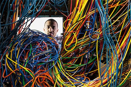simsearch:400-07167932,k - A black male technician working on a tangled mess of CAT 5 cables in a server room. Foto de stock - Sin royalties Premium, Código: 6118-09174317