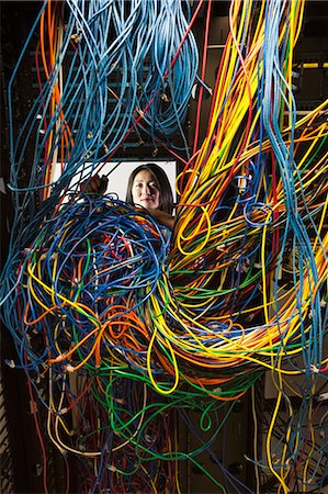 Asian female technician working on a tangled mess of CAT 5 cables in a server room. Stock Photo - Premium Royalty-Free, Code: 6118-09174316