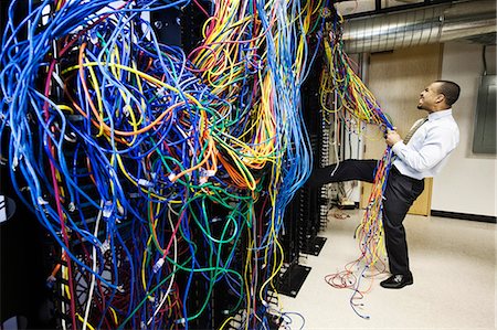 A black male technician pulling on a tangled mess of CAT 5 cables in a computer server room. Stock Photo - Premium Royalty-Free, Code: 6118-09174318