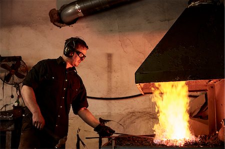 simsearch:6118-08729037,k - An artisan metal worker heating metal in a forge in his workshop. Foto de stock - Sin royalties Premium, Código: 6118-09174461