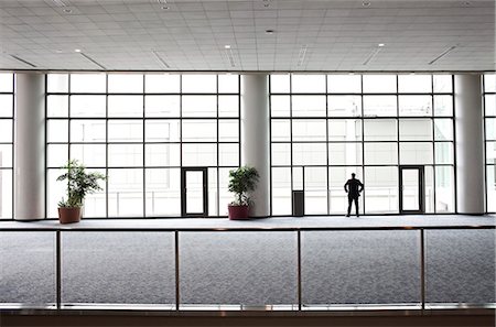 simsearch:6118-09174347,k - A businessman in silhouette standing at a large window in a convention centre lobby. Fotografie stock - Premium Royalty-Free, Codice: 6118-09174402