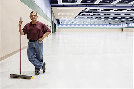 An Hispanic workman standing in a large interior space with a broom. Stock Photo - Premium Royalty-Free, Code: 6118-09174407