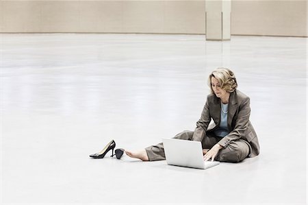 simsearch:6118-09174347,k - A Caucasian businesswoman working on a laptop computer while sitting on the floor of a convention centre arena. Fotografie stock - Premium Royalty-Free, Codice: 6118-09174408