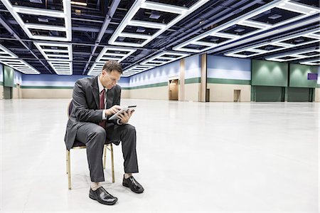 simsearch:6118-09173924,k - A Caucasian businessman texting while sitting in a chair in the middle of a convention centre arena. Stockbilder - Premium RF Lizenzfrei, Bildnummer: 6118-09174409
