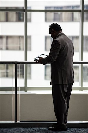 simsearch:6118-09174347,k - An Hispanic businessman using a notebook computer while standing in front of a window in a convention centre lobby. Fotografie stock - Premium Royalty-Free, Codice: 6118-09174413