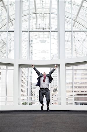 simsearch:6118-09174347,k - A businessman jumping for joy in front of a large window in a convention centre lobby. Fotografie stock - Premium Royalty-Free, Codice: 6118-09174410