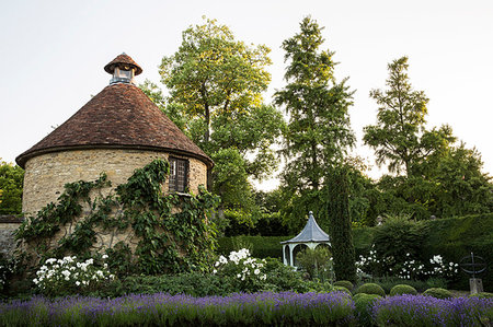 View of small round stone tower and pavilion from across a walled garden with trees and flowerbeds. Stockbilder - Premium RF Lizenzfrei, Bildnummer: 6118-09183440