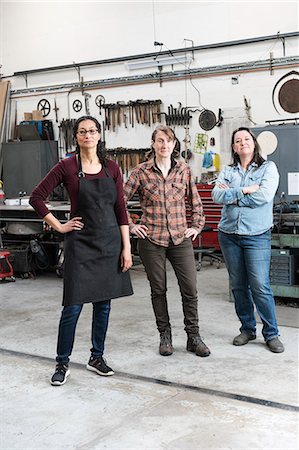 Three women standing in metal workshop, looking at camera. Stock Photo - Premium Royalty-Free, Code: 6118-09112000