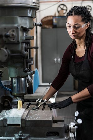 simsearch:6118-08202548,k - Woman wearing safety glasses standing in a metal workshop, working at a machine. Photographie de stock - Premium Libres de Droits, Code: 6118-09112014