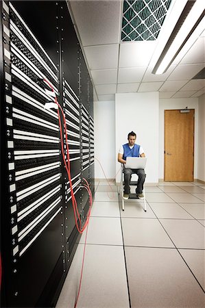 simsearch:6118-09129858,k - Computer technician working on a lap top computer while doing diagnostic work on a server in a larger computer server room. Foto de stock - Sin royalties Premium, Código: 6118-09129370