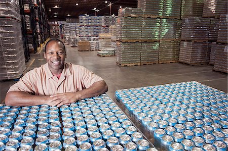 simsearch:6118-09129432,k - Portrait of an African American male warehouse foreman in a warehouse full of cans of flavoured water stored on pallets in the warehouse of a bottling plant. Fotografie stock - Premium Royalty-Free, Codice: 6118-09129440