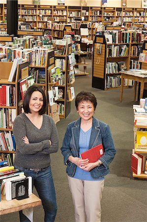 simsearch:6118-07354058,k - Portrait of  Caucasian female and Asian American female  owners of a large bookstore, showing multiple racks of books in the background. Stock Photo - Premium Royalty-Free, Code: 6118-09129472