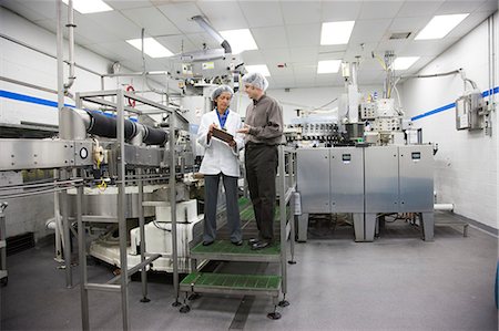 simsearch:6118-09129432,k - A discussion between a male Caucasian management person and a female African American technician in the bottling area of a bottled water plant. Fotografie stock - Premium Royalty-Free, Codice: 6118-09129412