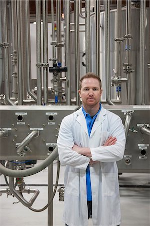 simsearch:6118-09129432,k - Caucasian male technician in a white coat standing near large stainless steel processing tanks in a bottling plant that makes flavoured water . Fotografie stock - Premium Royalty-Free, Codice: 6118-09129415